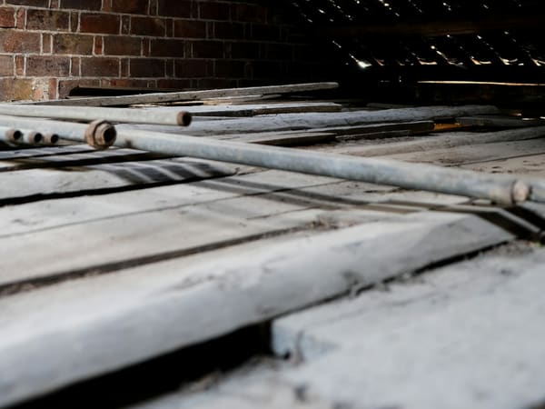 The inside of an old roof space with a brick chimney, exposed timber rafters and daylight showing through the tiles. No insulation.